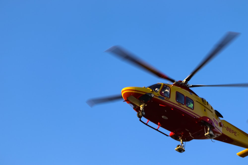 a red and yellow helicopter flying through a blue sky