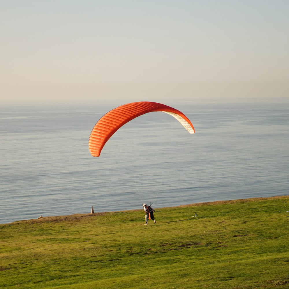a person flying a large orange kite over a lush green field