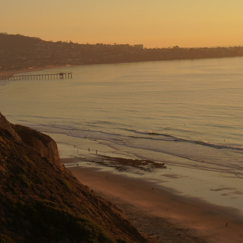 a view of a beach at sunset with a pier in the distance