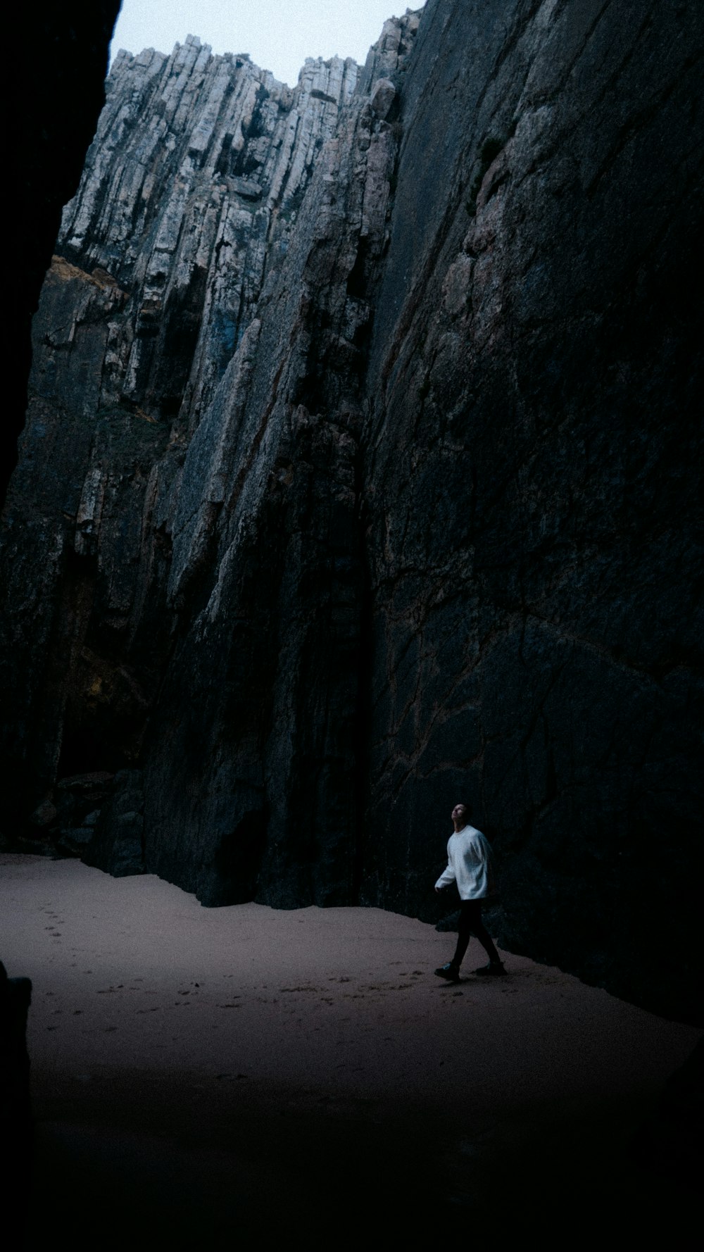 a man walking on a beach next to a large rock formation