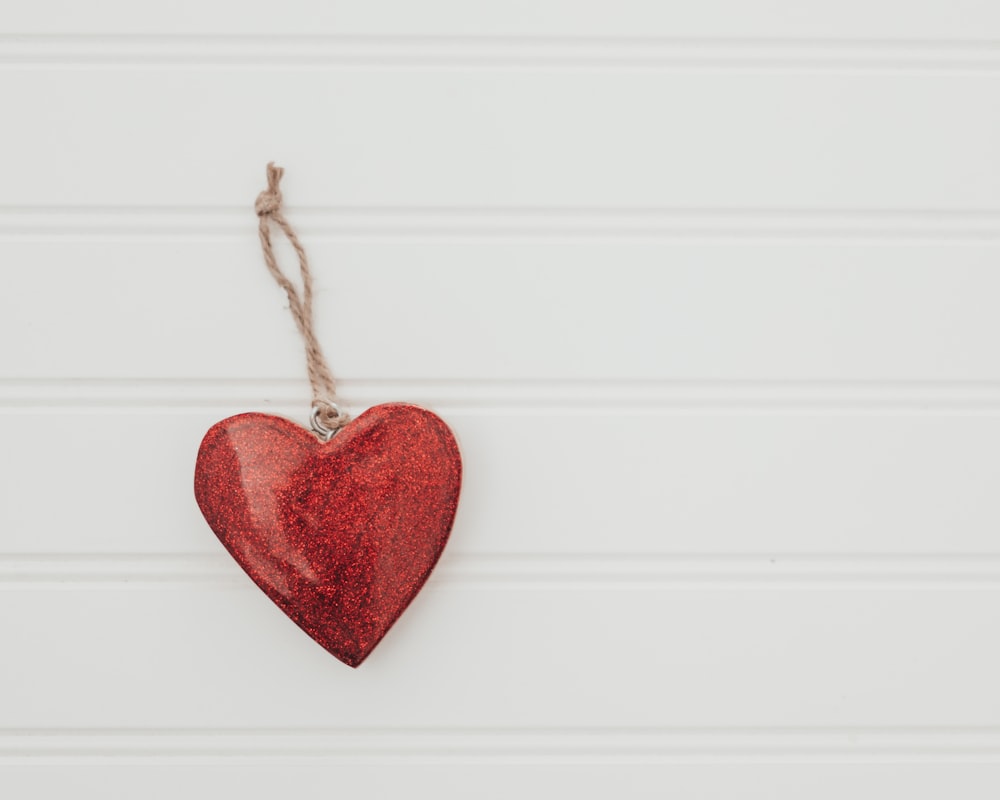 a red heart hanging from a string on a white wall