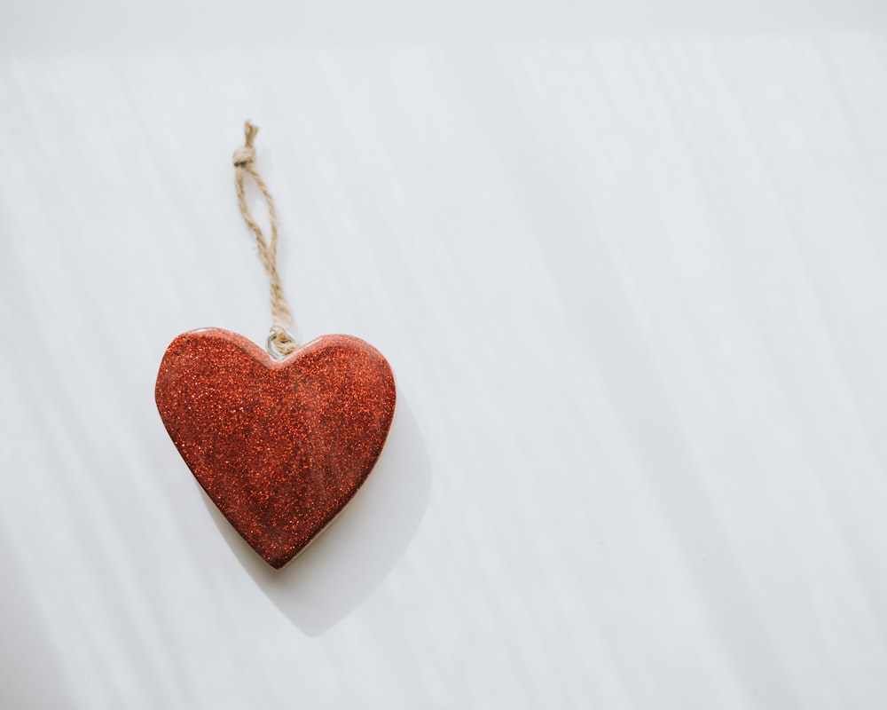a red heart hanging from a string on a white wall