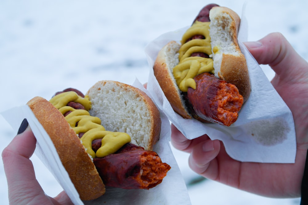 a person holding a hot dog in a bun with mustard and ketchup