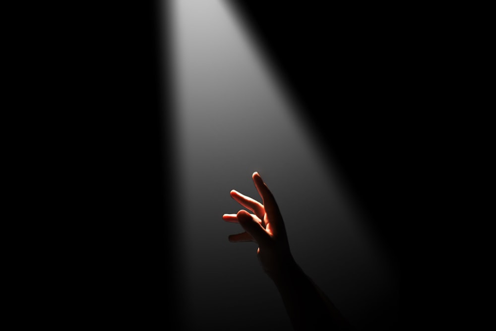a person's hand reaching up towards a light