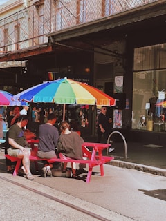 a group of people sitting on a red bench under an umbrella