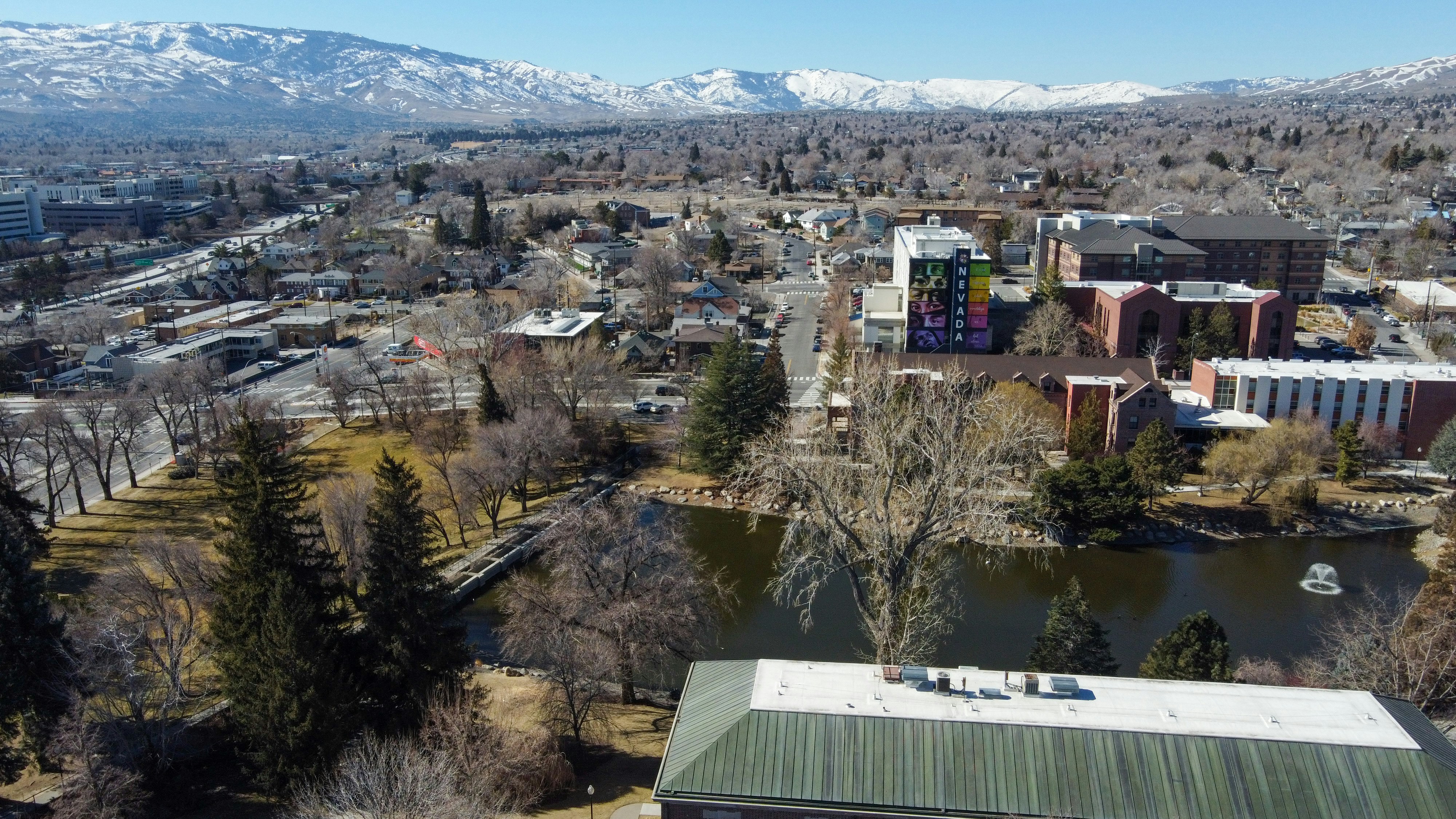 Reno from above in winter, with brick buildings, a pond ringed by bare trees and snow-covered mountains along the horizon under a clear sky