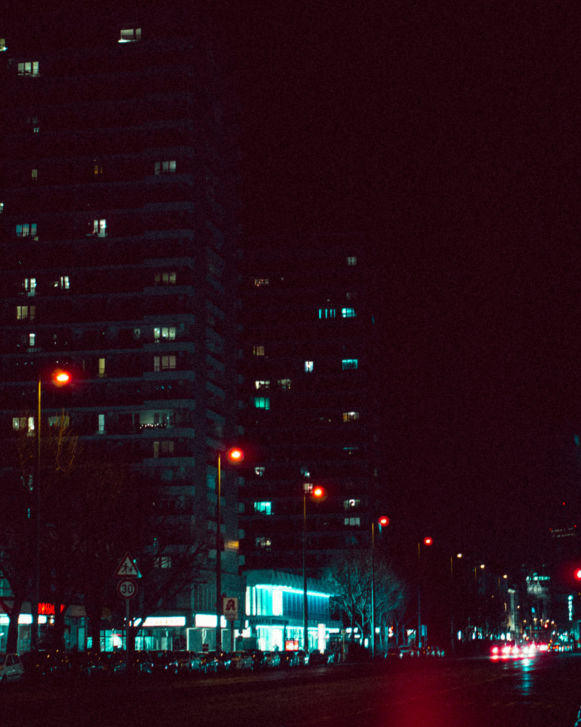 A minimalist urban scene at night, with sharp contrasts between dark buildings and glowing streetlights.