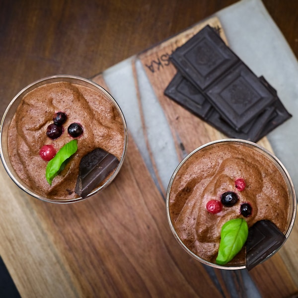 two glasses filled with chocolate pudding on top of a wooden table