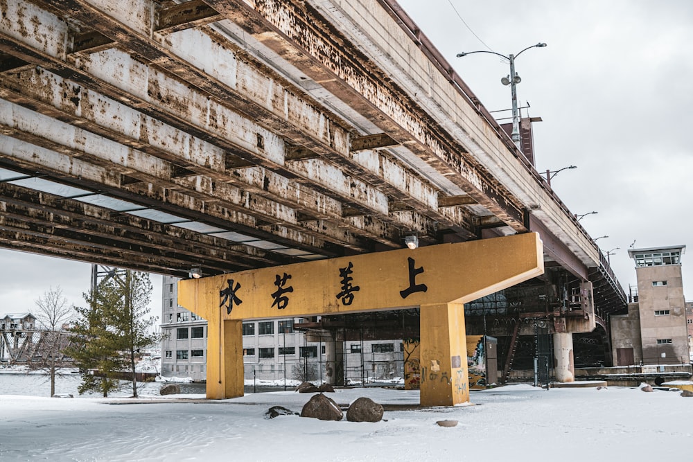 a yellow sign that is under a bridge