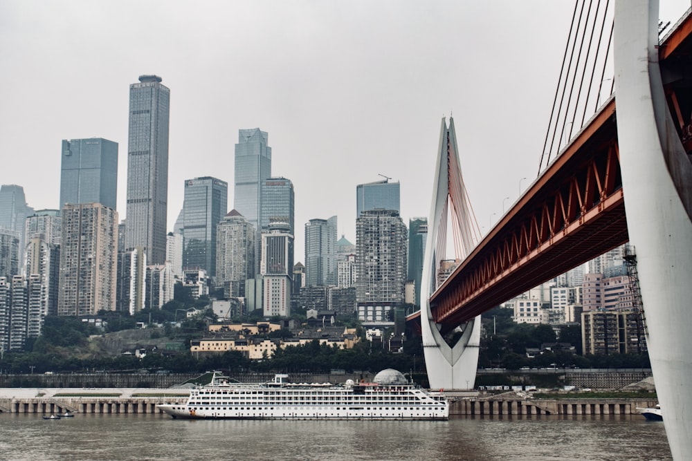 a cruise ship passing under a bridge with a city in the background