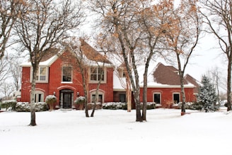 a red brick house surrounded by trees and snow