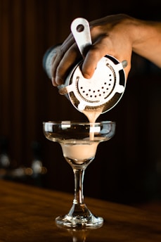 a person pours a drink into a martini glass