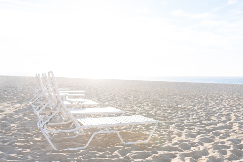 a row of white lawn chairs sitting on top of a sandy beach