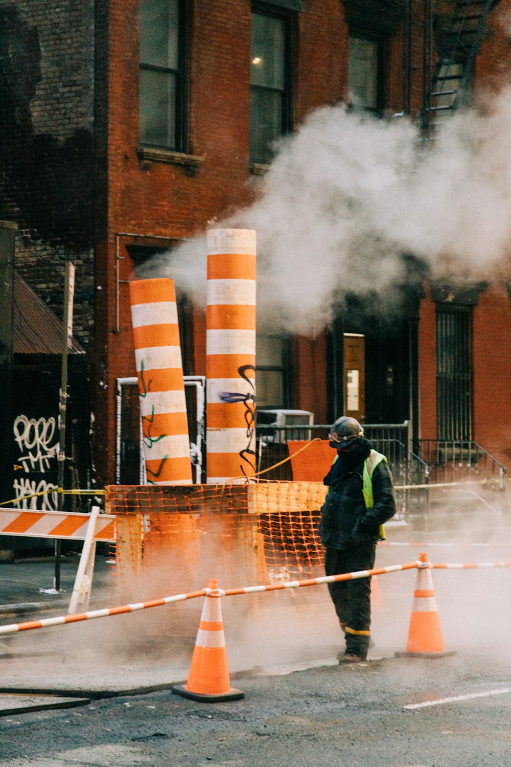 a man in a black jacket standing next to orange cones