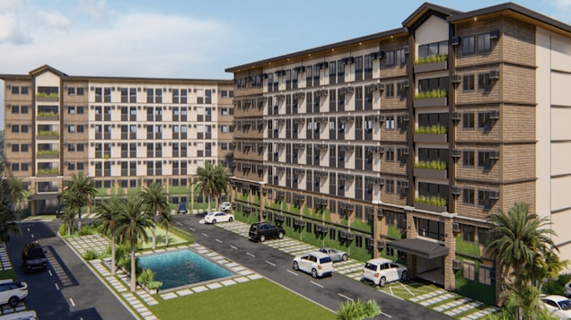 A modern apartment complex featuring two multi-story buildings with large windows and balconies. The complex is surrounded by landscaped areas with palm trees and a small pool in the center. Several parked vehicles are situated along the paved driveway that runs between the buildings.