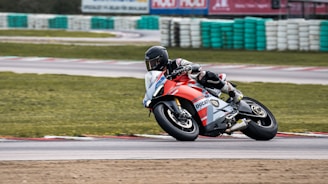 A dynamic shot of a motorcyclist wearing a reinforced racing suit, speeding on a winding track under a clear sky.