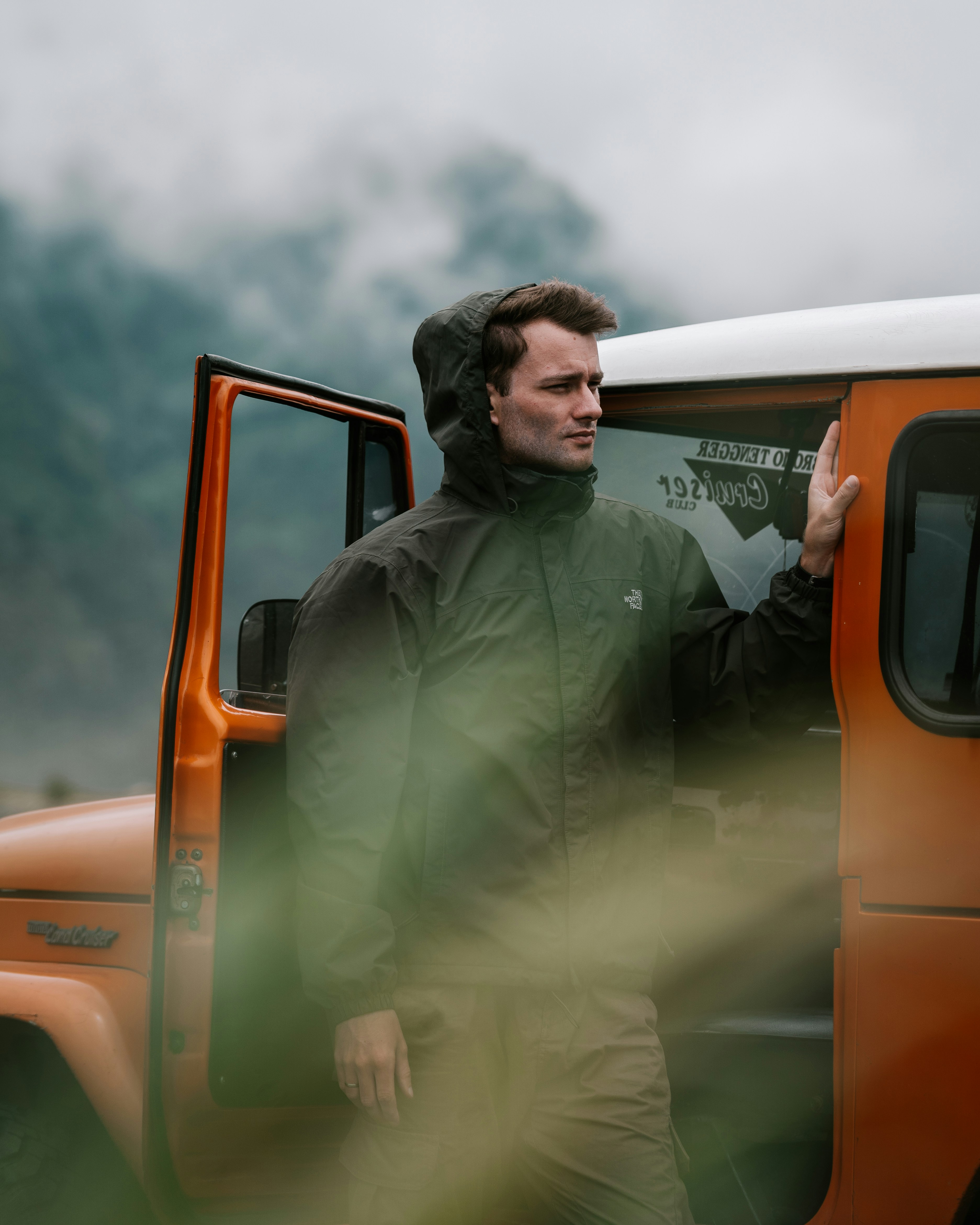 a man in a green jacket standing next to an orange truck