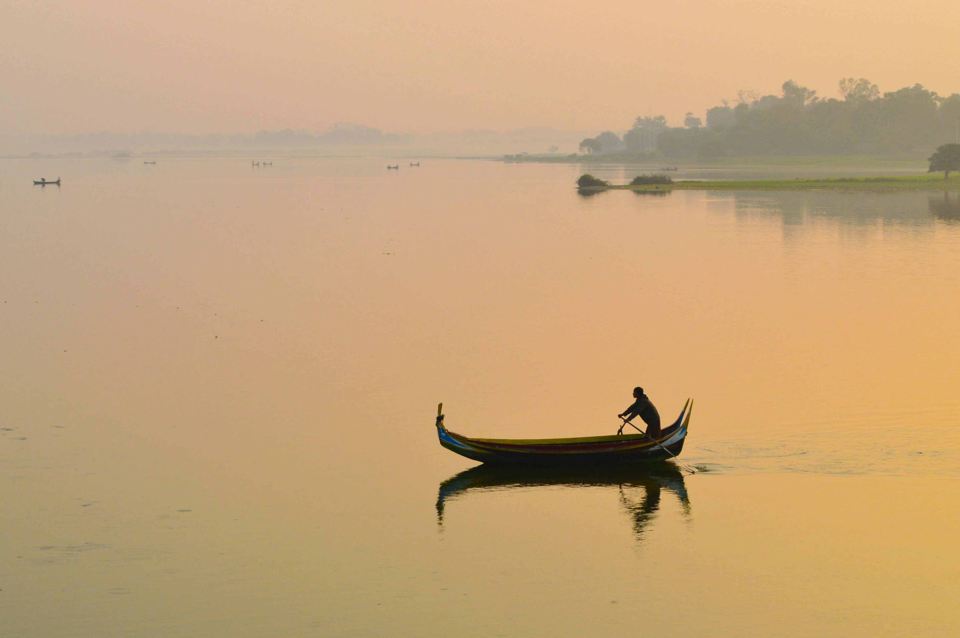 Man paddling boat reflected in water at sunrise