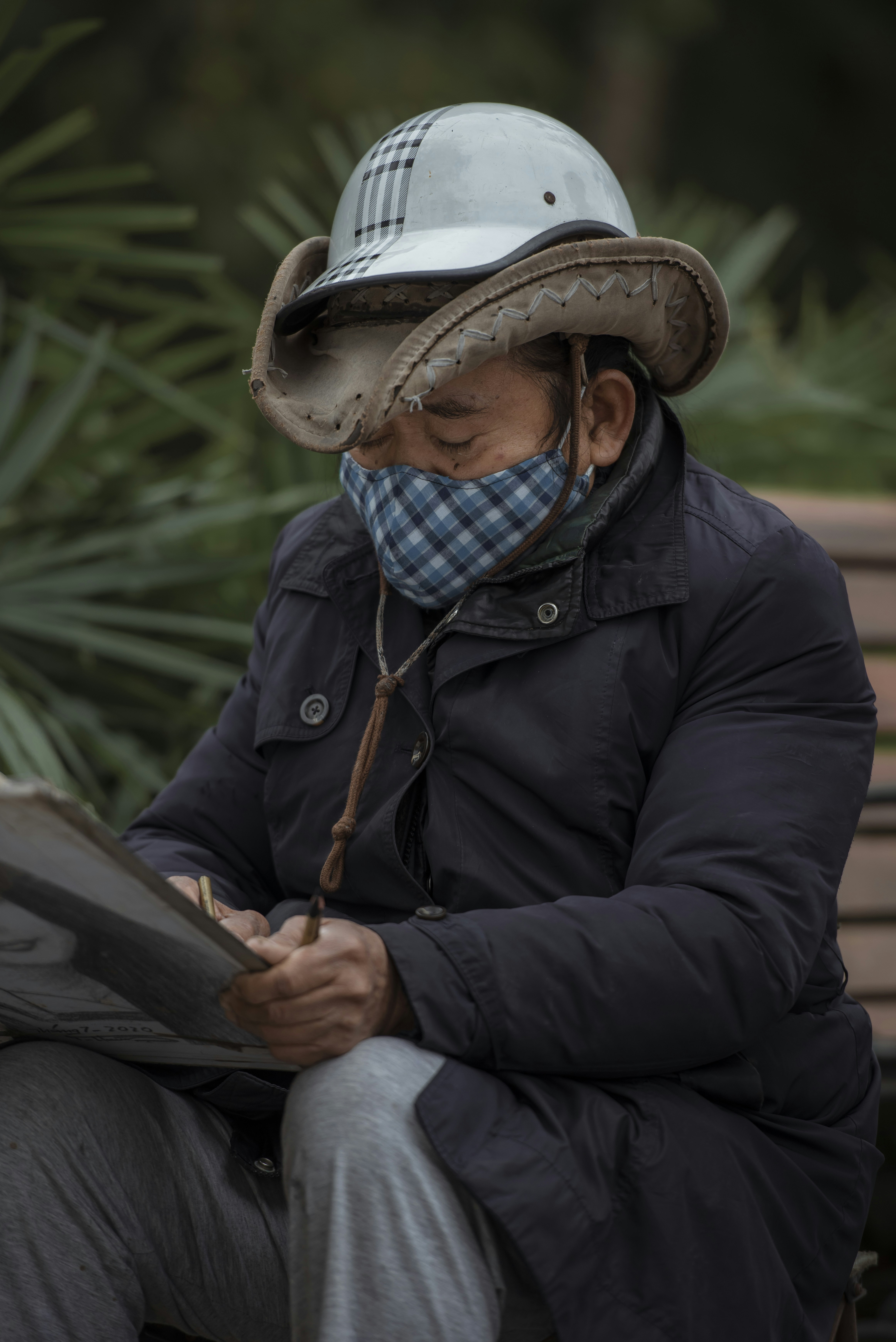 um homem sentado em um banco usando um chapéu e segurando uma prancheta