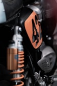 Close-up view of a motorcycle focusing on the details of its suspension system and a panel with the number 42 marked in orange. The image highlights metallic components, including the shock absorber, and uses shallow depth of field to emphasize specific parts.
