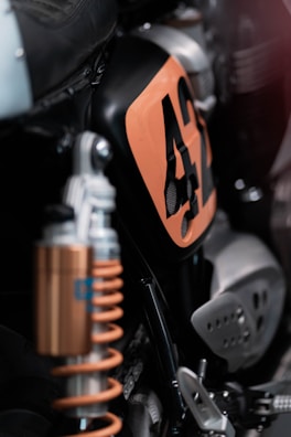 Close-up view of a motorcycle focusing on the details of its suspension system and a panel with the number 42 marked in orange. The image highlights metallic components, including the shock absorber, and uses shallow depth of field to emphasize specific parts.