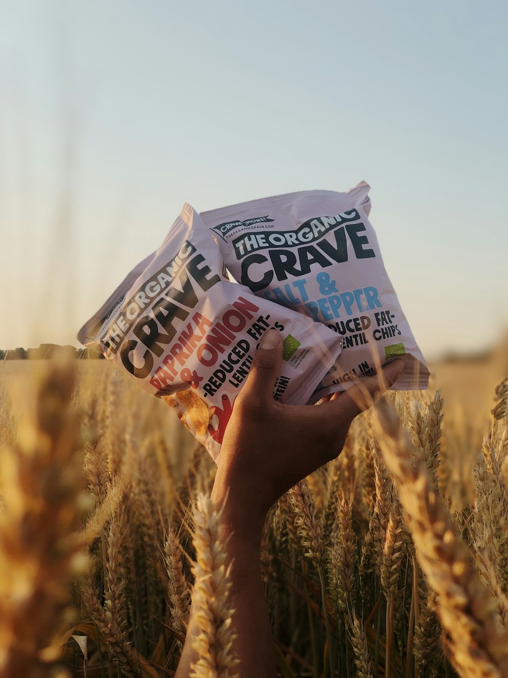 a hand holding a bag of crave next to a wheat field