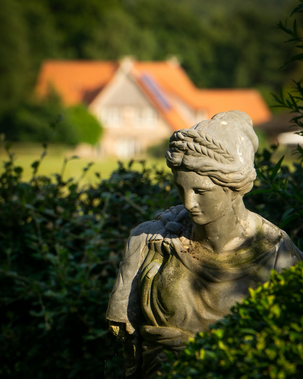 a statue of a woman in a garden with a house in the background