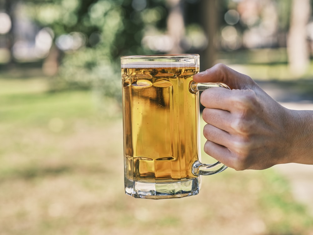a person holding a mug of beer in a park