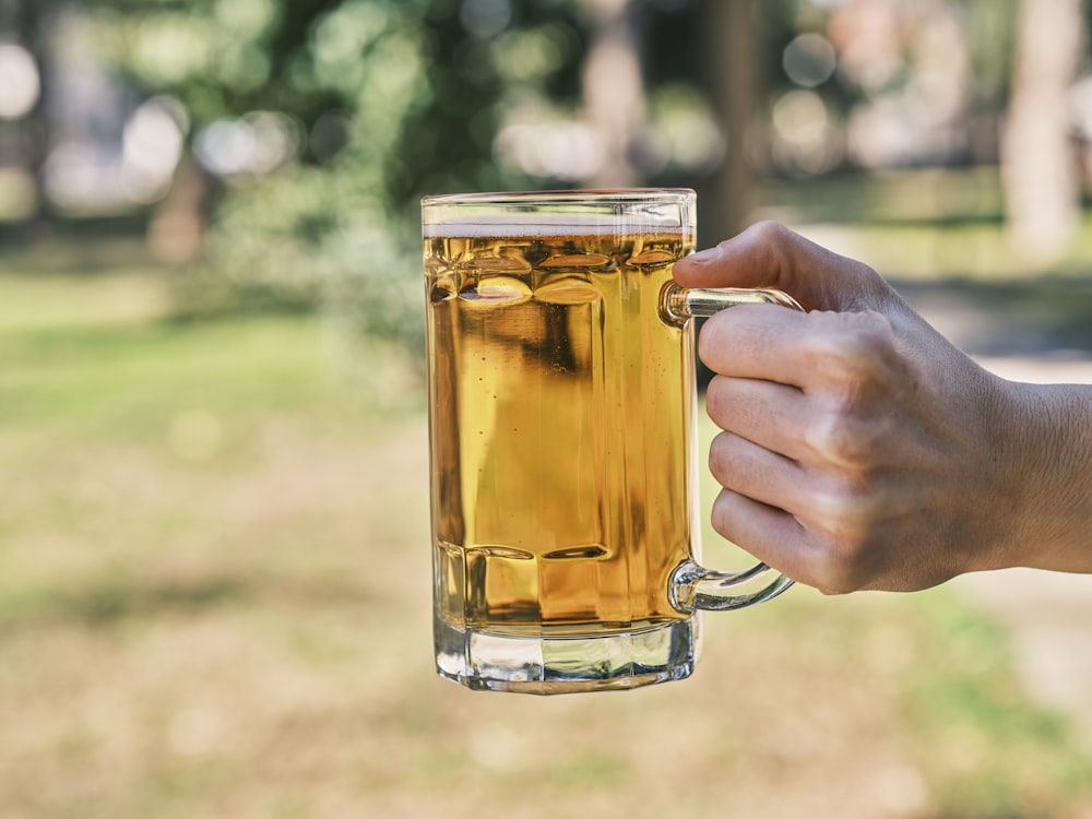 Una persona sosteniendo una jarra de cerveza en un parque