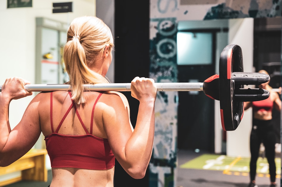 Woman in a red sports bra with a loaded barbell across her upper back, seen from behind