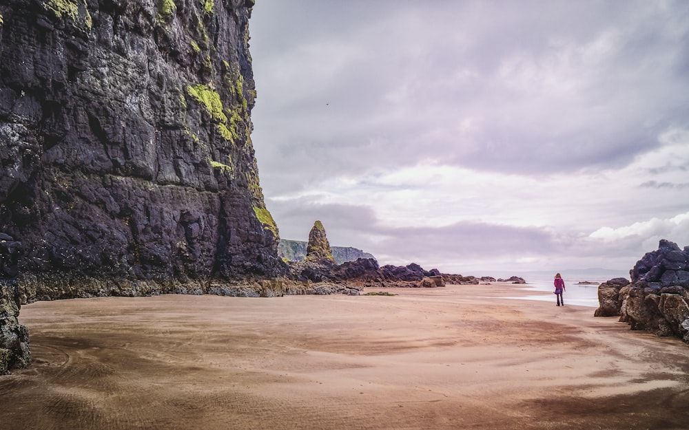 a person standing on a beach next to a cliff