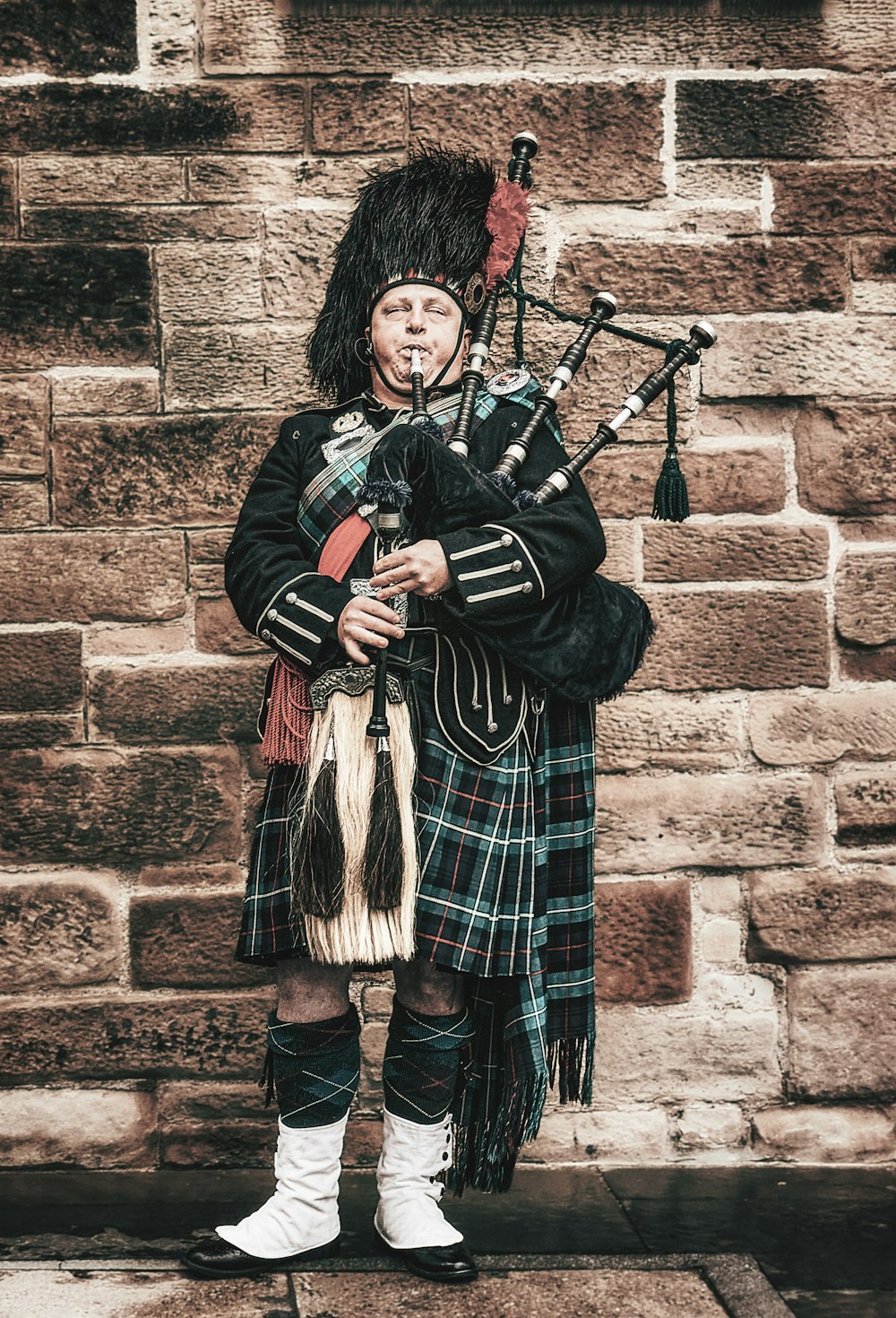 a man in a kilt standing in front of a brick wall