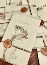 A collection of elegantly wrapped envelopes tied with twine and adorned with dried flowers and wax seals featuring a rose design. The envelopes are arranged casually on a wooden surface, creating a vintage and romantic ambiance.