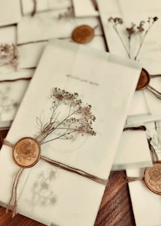 A collection of elegantly wrapped envelopes tied with twine and adorned with dried flowers and wax seals featuring a rose design. The envelopes are arranged casually on a wooden surface, creating a vintage and romantic ambiance.