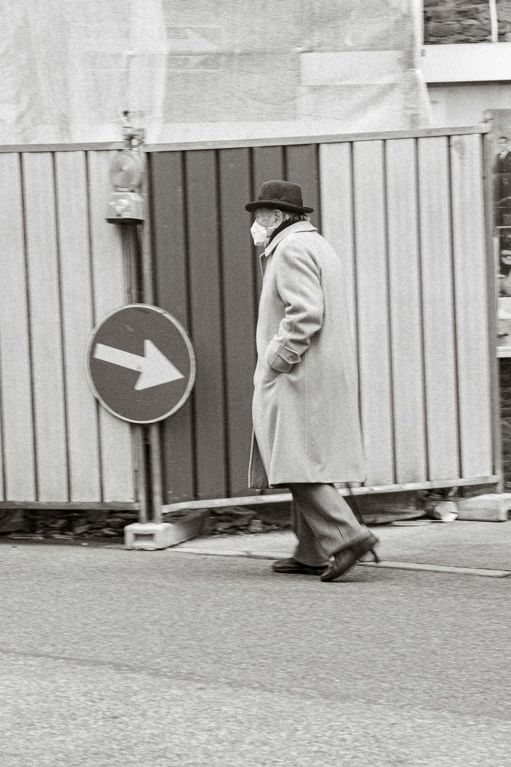 a man in a coat and hat walking down a street