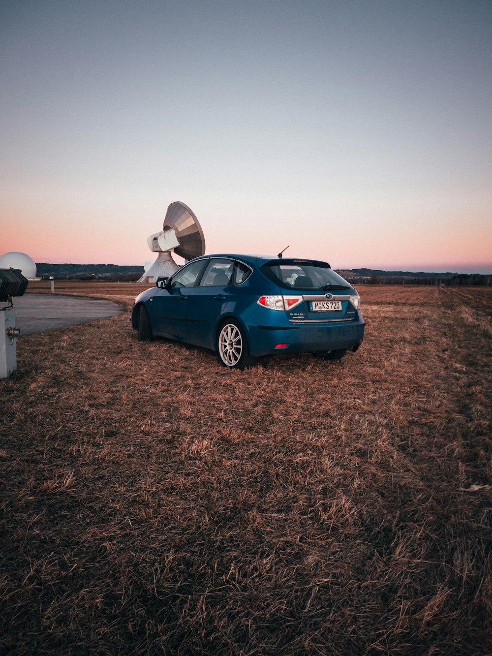 a blue car parked on top of a dry grass field