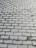 Gray cobblestone pavement arranged in a uniform pattern. The surface appears slightly wet, with darker areas indicating moisture. The bricks are rectangular, consistently aligned, and there is a slight glint from the surface.