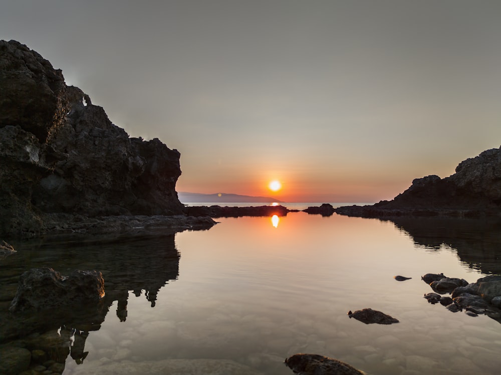 un cuerpo de agua rodeado de rocas y una puesta de sol