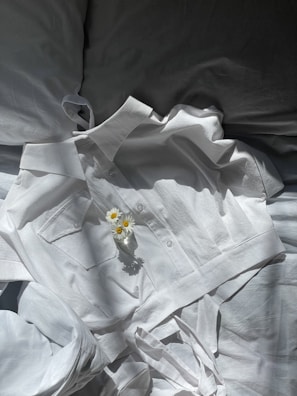 Ivelli pyjamas folded neatly next to a small vase with fresh flowers on a white bedside table.