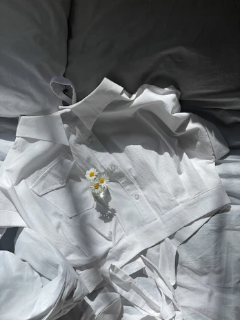A neat pile of folded clothes with a small vase of fresh flowers on a light wooden table.
