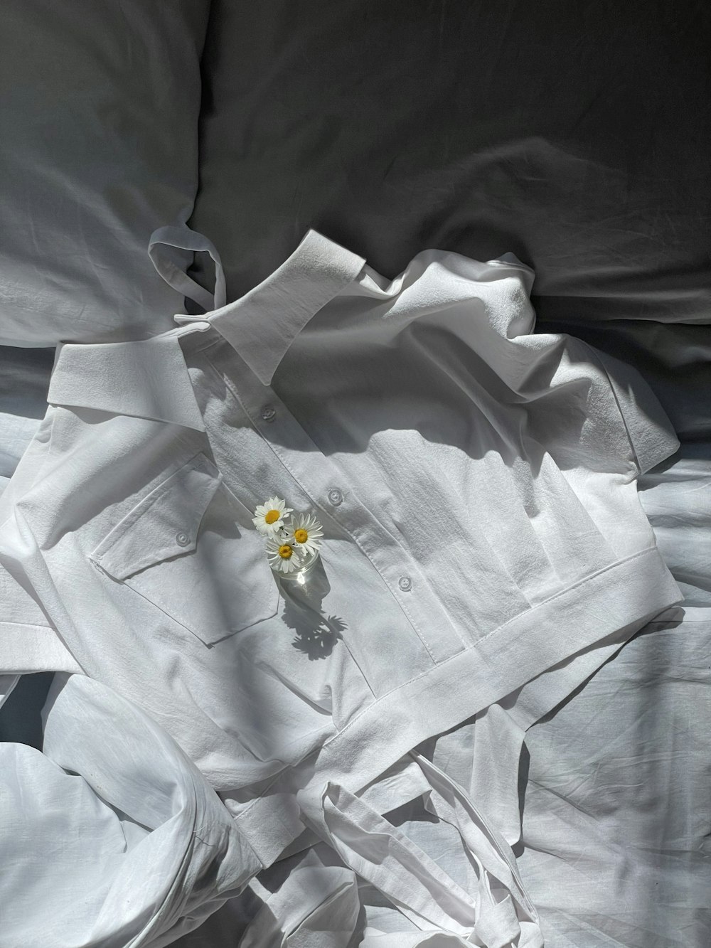 a white shirt laying on top of a bed next to a flower