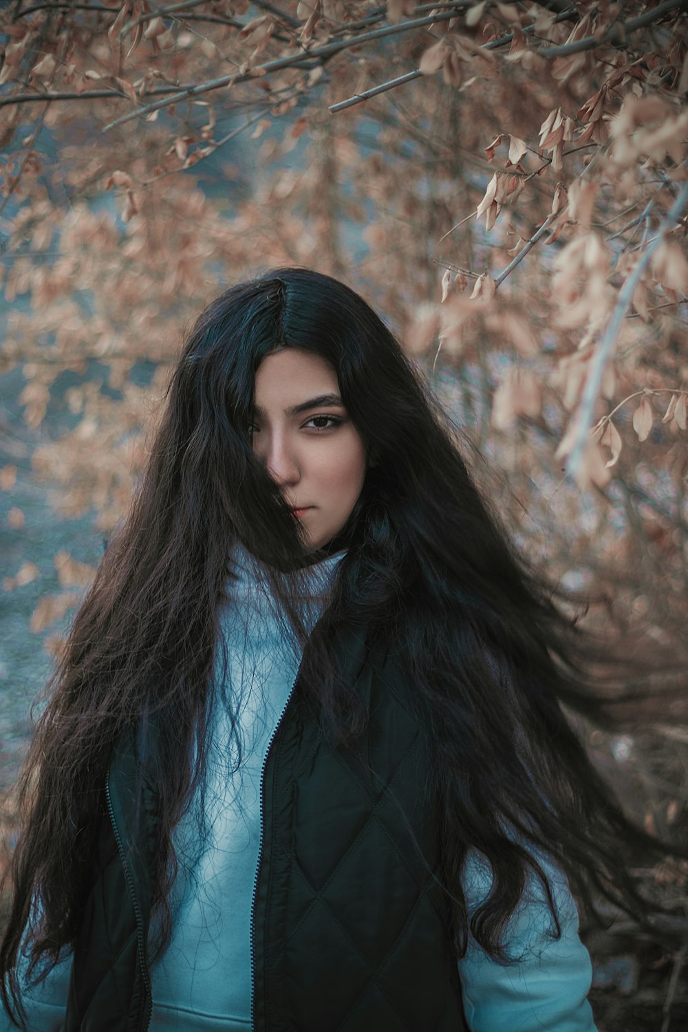 a woman with long black hair standing in front of a tree