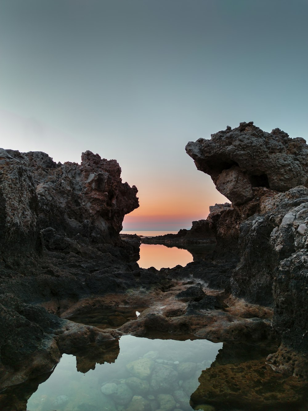 the sun is setting over the water and rocks