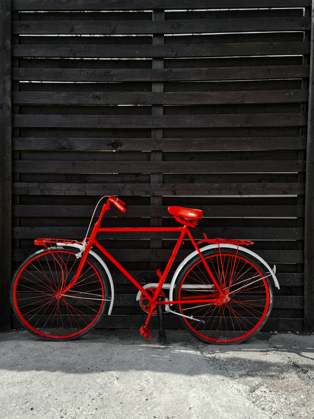 a red bicycle parked next to a wooden fence