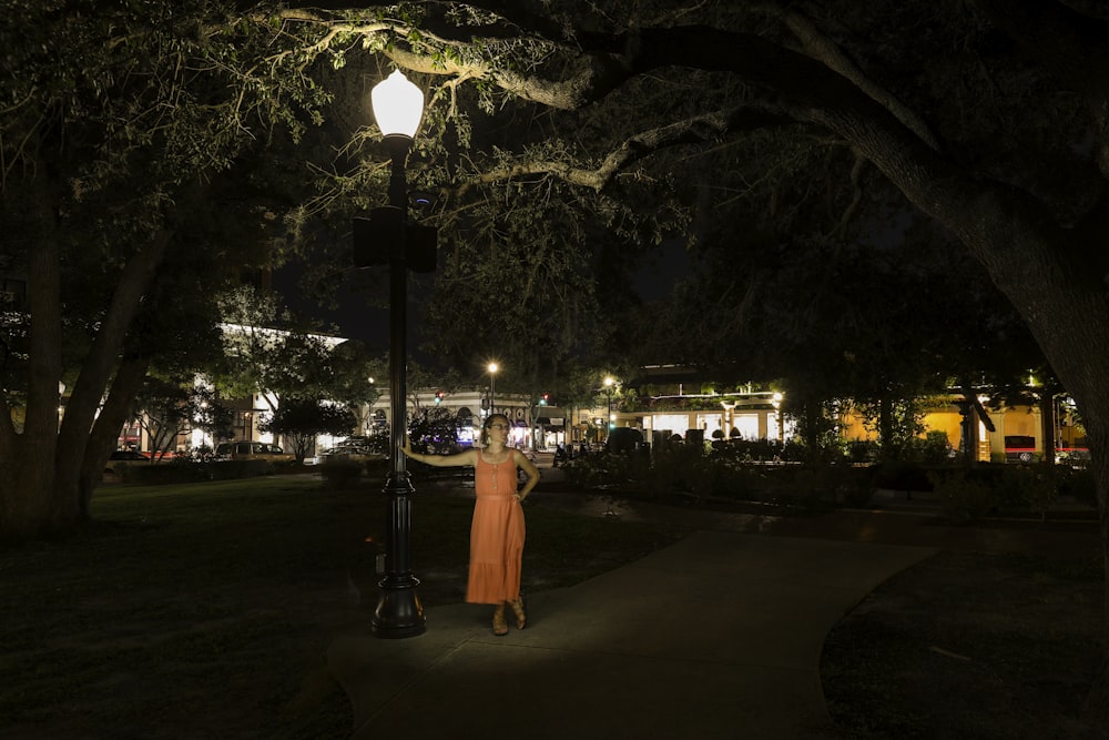 uma mulher em um vestido laranja de pé sob uma luz de rua