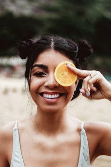 a woman holding an orange slice up to her eye