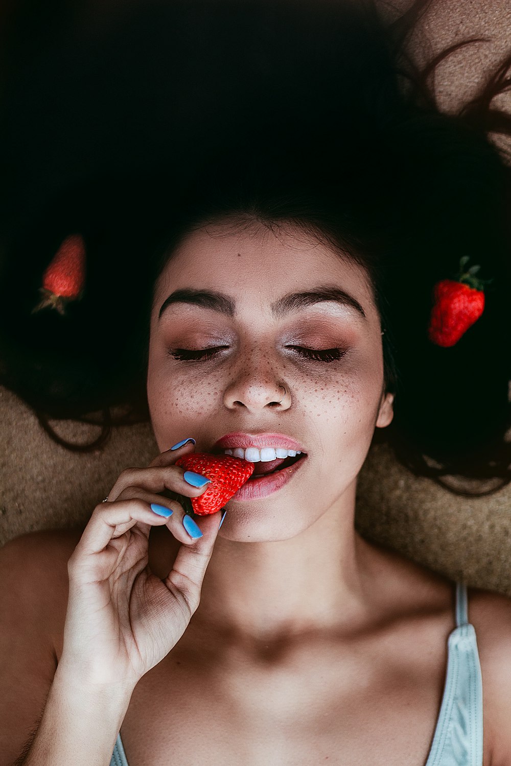 a woman laying down with a strawberry in her mouth