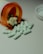 Several white capsules with numbers are scattered across a surface, with an orange prescription bottle lying on its side. The pills spill out of the container, and a white bottle cap is visible nearby.