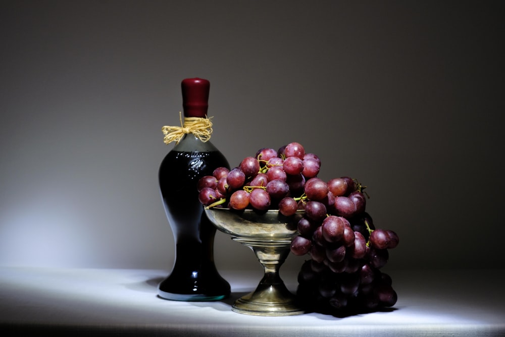 a bottle of wine next to a bowl of grapes