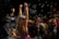 Children are gathered in a dark environment, with one child in the foreground raising arms surrounded by bubbles. Neon bracelets and colorful outfits suggest a festive atmosphere. Multiple children, some of whom seem to be playing, are involved in what looks like a party or event.